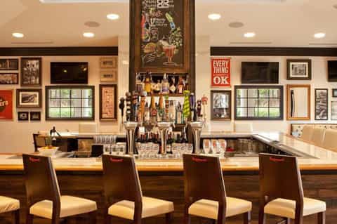 Hotel bar with vintage decor, framed photographs, bottles, and seating for guests