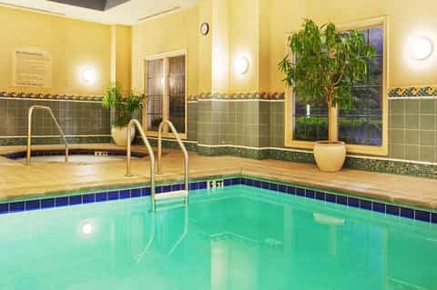 Indoor spa pool with yellow walls, green tile accents, and ladder entry