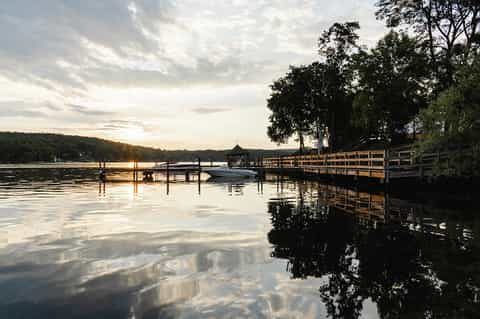 Lakeside dock at dusk with boat, wooden pier, and tree-lined shoreline