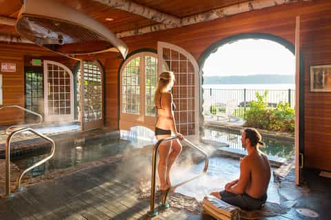 Indoor-outdoor hot spring bath with wooden architecture overlooking calm lake and mountains