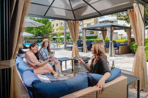 Three women chatting under pergola with fire pit at resort pool area