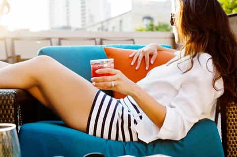 Woman relaxing on blue and orange couch with cocktail overlooking city skyline
