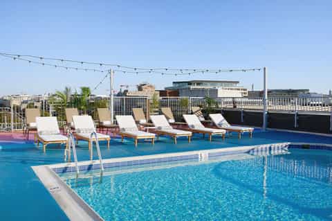 Rooftop pool deck with white loungers, string lights, and urban waterfront city skyline