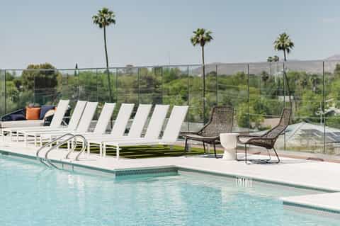 Resort pool with white loungers, glass railing, palm trees, and scenic hillside valley views