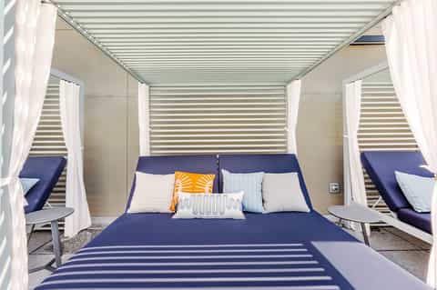 Modern canopy bed with navy bedding, white curtains, and striped ceiling inside resort cabana