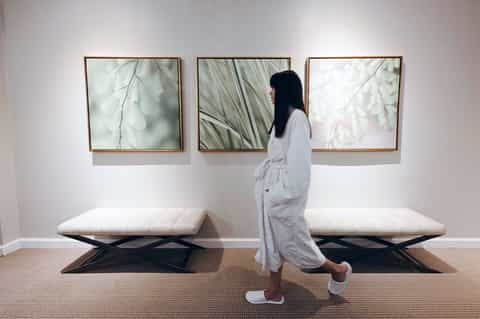 Spa corridor with woman viewing three framed botanical prints above white upholstered benches