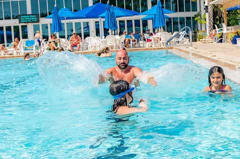 Father and children swimming and playing in resort pool on sunny day
