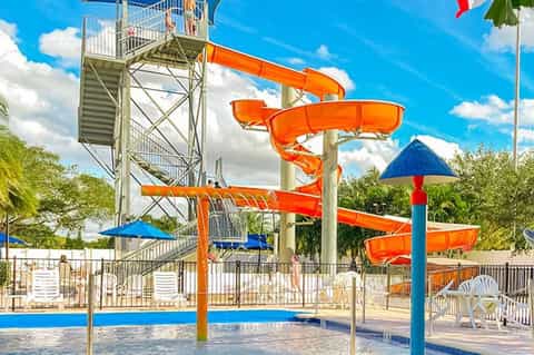 Colorful water park with orange tube slides, blue umbrellas, tall slide tower, and shallow pool area