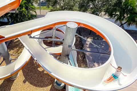 Curved white water slide at resort pool area with tropical plants visible