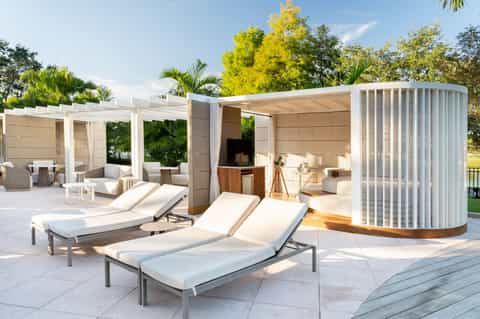 Luxury spa cabana with lounge chairs, pergolas, striped privacy screens, and manicured landscaping