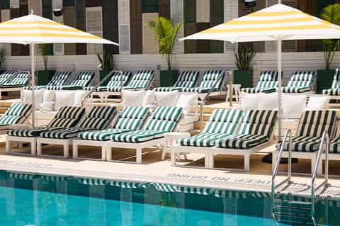 Resort poolside with green and white striped lounge chairs, yellow umbrellas, and cabanas