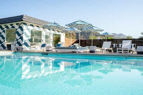 Contemporary pool area with striped umbrellas, modern cabana, mountain views, and pristine turquoise water
