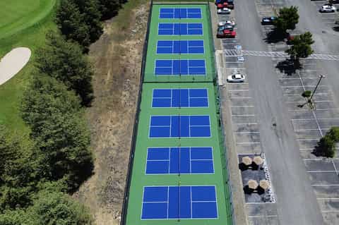 Multiple blue and green pickleball courts viewed from above with parking lot and trees