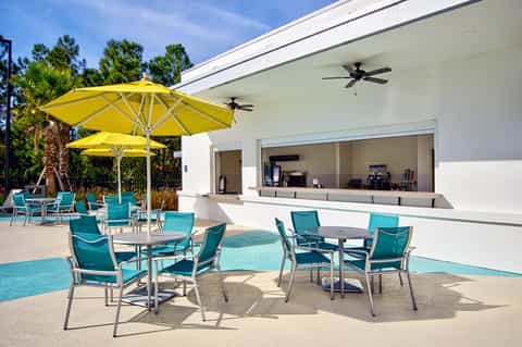 Outdoor patio with turquoise chairs, yellow umbrella, and modern white building with bar