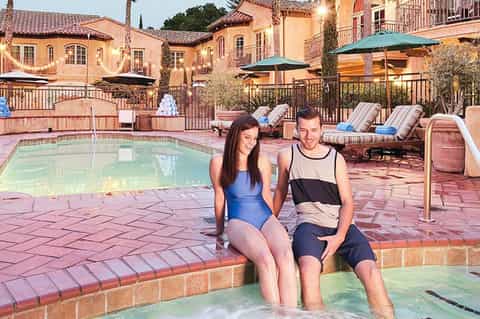 Mediterranean-style resort pool with spa, loungers, terracotta buildings, and evening lighting