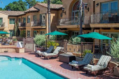 Spanish-style resort courtyard with turquoise pool, lounge chairs, green umbrellas, and terracotta tiles
