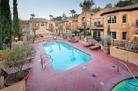 Mediterranean-style resort courtyard with terracotta pool, arched architecture, lounge chairs, and landscaping