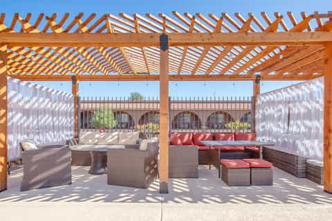 Wooden pergola lounge area with wicker furniture and sheer white curtains on a patio