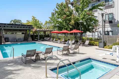 Rectangular pool with lounge chairs, red umbrellas, and pergola-covered patio area