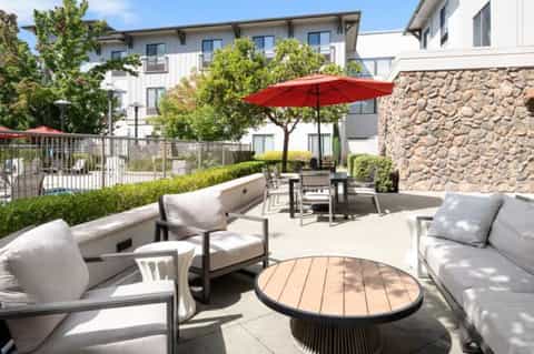 Outdoor patio lounge area with comfortable seating, red umbrella, and stone accent wall