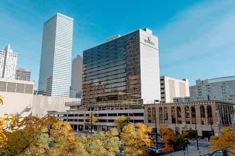 Downtown urban hotel building with glass windows surrounded by skyscrapers and autumn trees