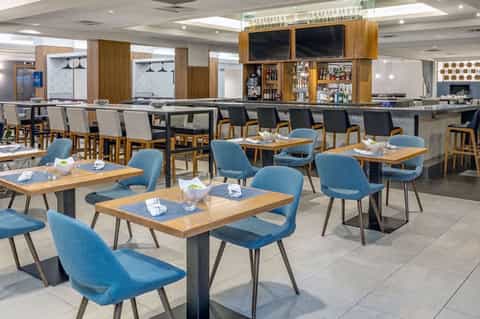 Modern dining room with wood tables, blue chairs, and full-service bar