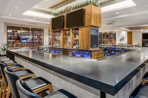Modern hotel bar with wooden display cabinet, metal countertop, bar seating, and multiple beverage selections