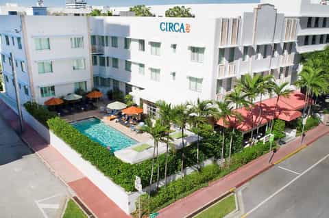 Modern white resort building exterior with pool, orange umbrellas, and palm tree landscaping