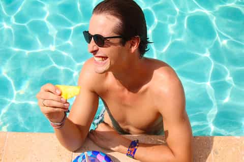 Man enjoying frozen popsicle in resort pool wearing sunglasses and colorful wristbands