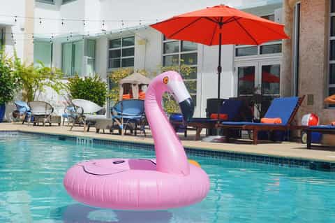 Resort pool with pink flamingo float, lounge chairs, red umbrella, and modern building