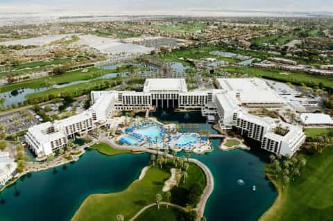 Aerial view of large resort with multiple white buildings, pools, surrounding golf courses and water features