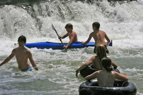 Children playing in ocean waves with blue and black inflatable tubes and floats