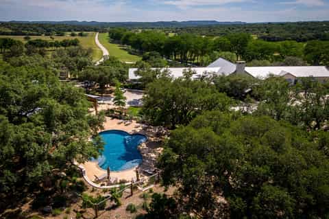 Aerial view of luxury resort pool nestled in trees with white buildings and river