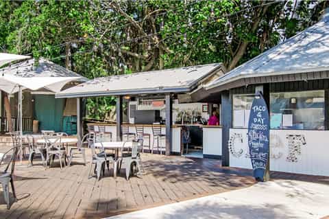 Beachside casual restaurant with outdoor seating and taco bar under mature trees