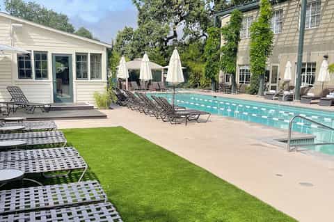 Contemporary pool area with mint-green water, white umbrellas, ivy-covered buildings, and green lawn