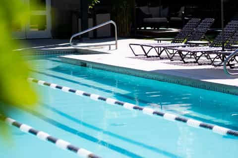 Lap pool with lane dividers, lounge chairs, metal railings, and modern architecture