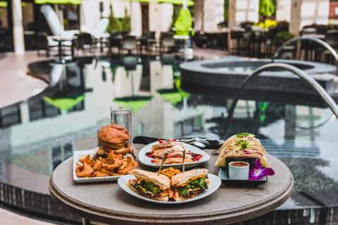 Resort poolside dining table with burgers, appetizers, and water glasses overlooking hot tubs