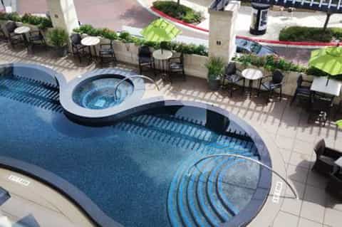 Overhead view of curved swimming pool with spa, surrounding seating areas and green umbrellas
