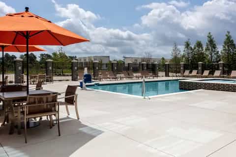 Resort pool with orange umbrellas, lounge chairs, and brick fence at dusk