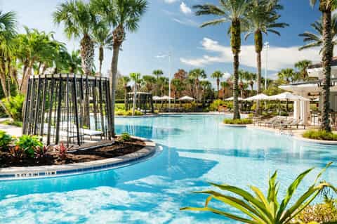 Expansive resort pool with black cabanas, lush landscaping, palm trees, and covered seating areas