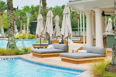 Luxurious poolside cabanas with cream umbrellas, wooden daybeds, and resort landscape