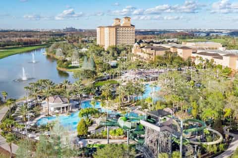 Aerial view of sprawling resort with multiple pools, water slides, hotel towers, and lake
