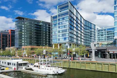 Waterfront development with modern residential towers, boats, and public plaza overlooking harbor