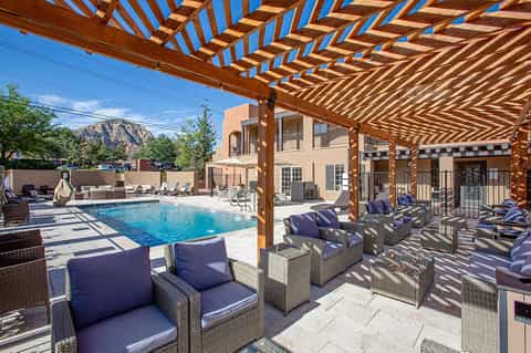 Resort pool deck with wooden pergola, loungers, and mountain views in sunny desert setting
