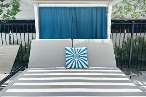 Modern cabana bed with white cushions and blue curtain backdrop on rooftop terrace