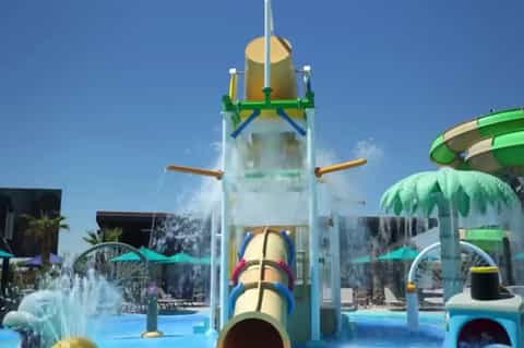 Colorful water park with tall blue splash tower, water slides, umbrellas, and clear blue sky