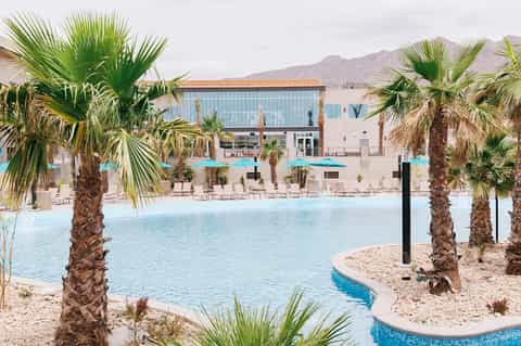 Resort lagoon pool surrounded by palm trees with turquoise umbrellas and modern building