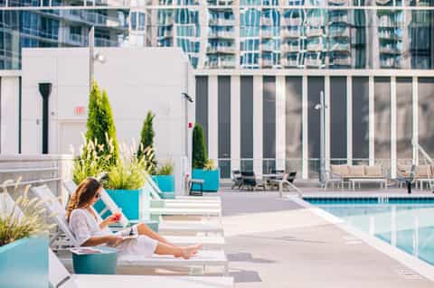 Woman relaxing on lounge chair by rooftop pool with modern high-rise buildings in background