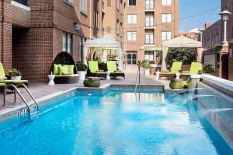 Urban rooftop pool with lime green loungers, umbrellas, and brick apartment buildings surrounding
