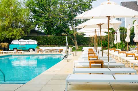 Poolside loungers with white umbrellas, vintage turquoise van, and manicured grounds